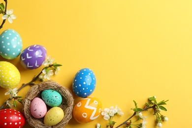 Photo of Flat lay composition with painted Easter eggs and blossoming branches on color background, space for text