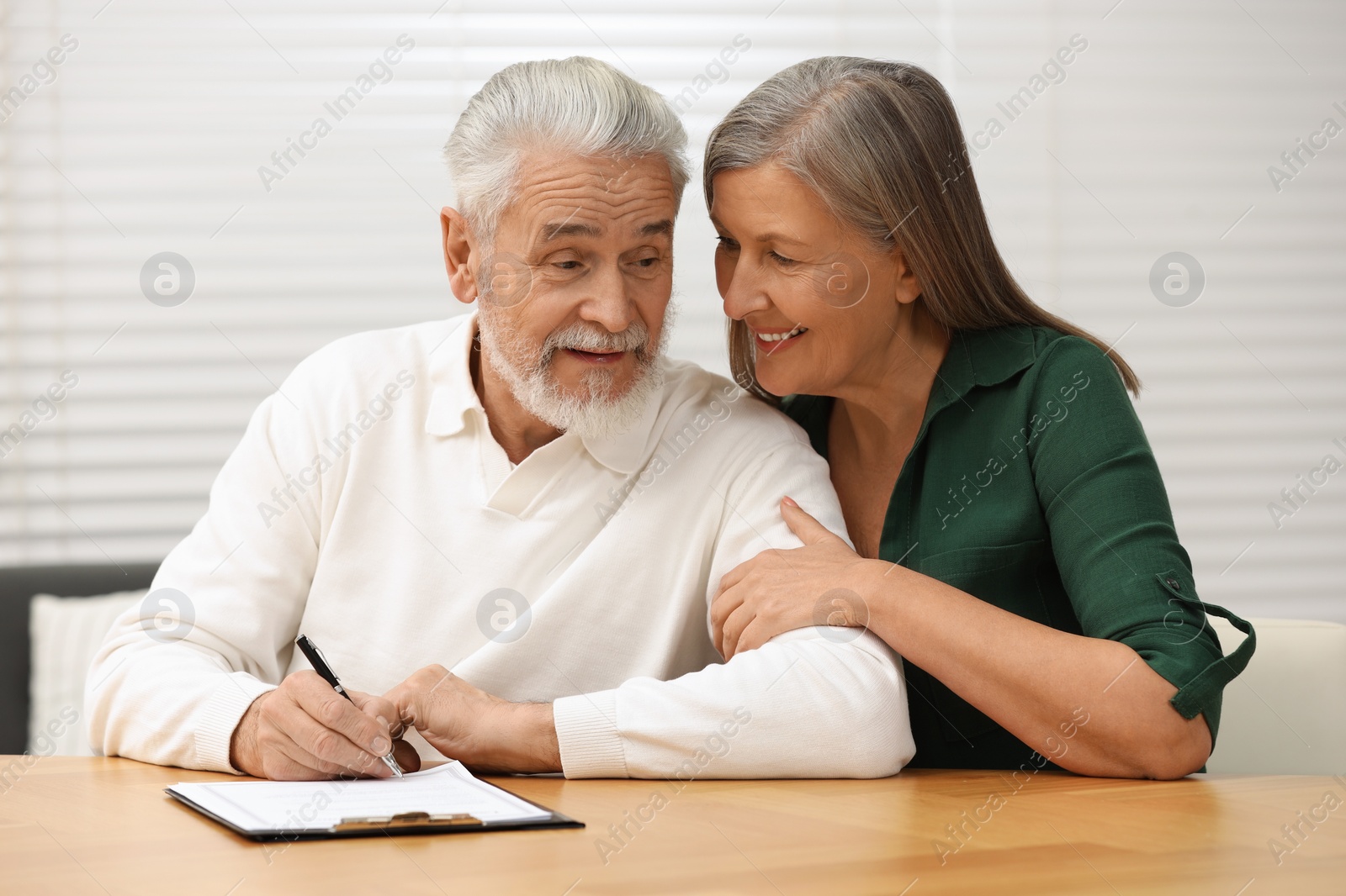 Photo of Senior couple signing Last Will and Testament indoors