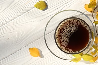 Cup of hot drink and leaves on white wooden table, flat lay with space for text. Cozy autumn atmosphere