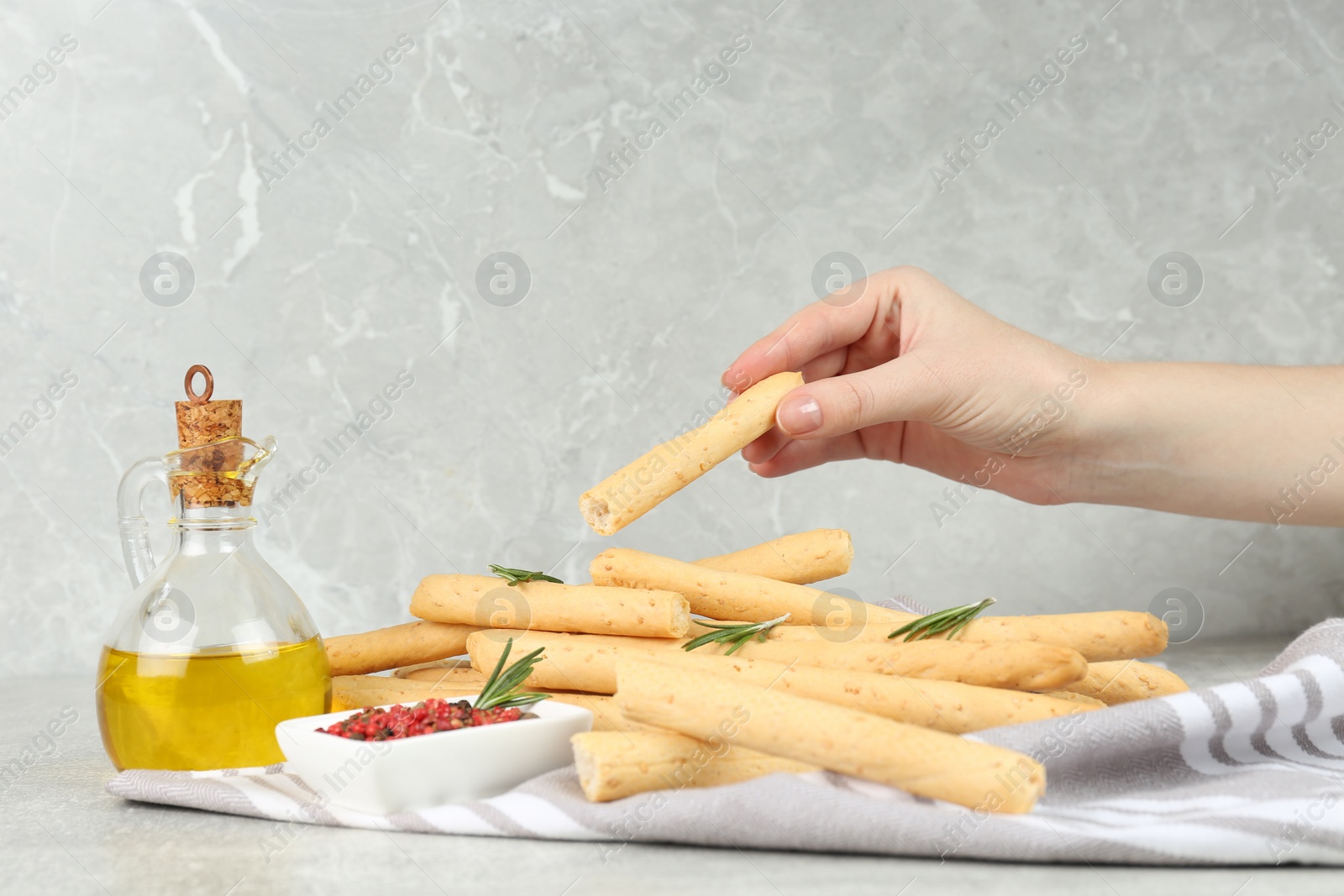 Photo of Woman eating tasty grissini at light grey table, closeup