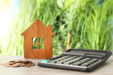 Photo of Wooden house model, calculator and coins on table outdoors