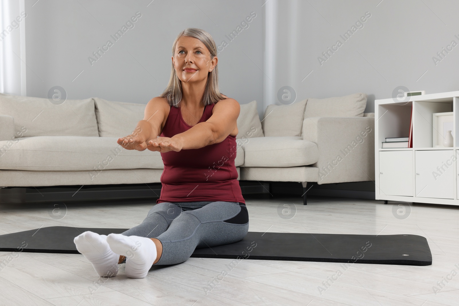 Photo of Senior woman in sportswear stretching on fitness mat at home, space for text