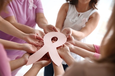 Women holding pink paper ribbon, closeup. Breast cancer awareness concept