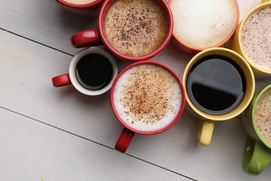 Many different cups with aromatic hot coffee on white wooden table, flat lay