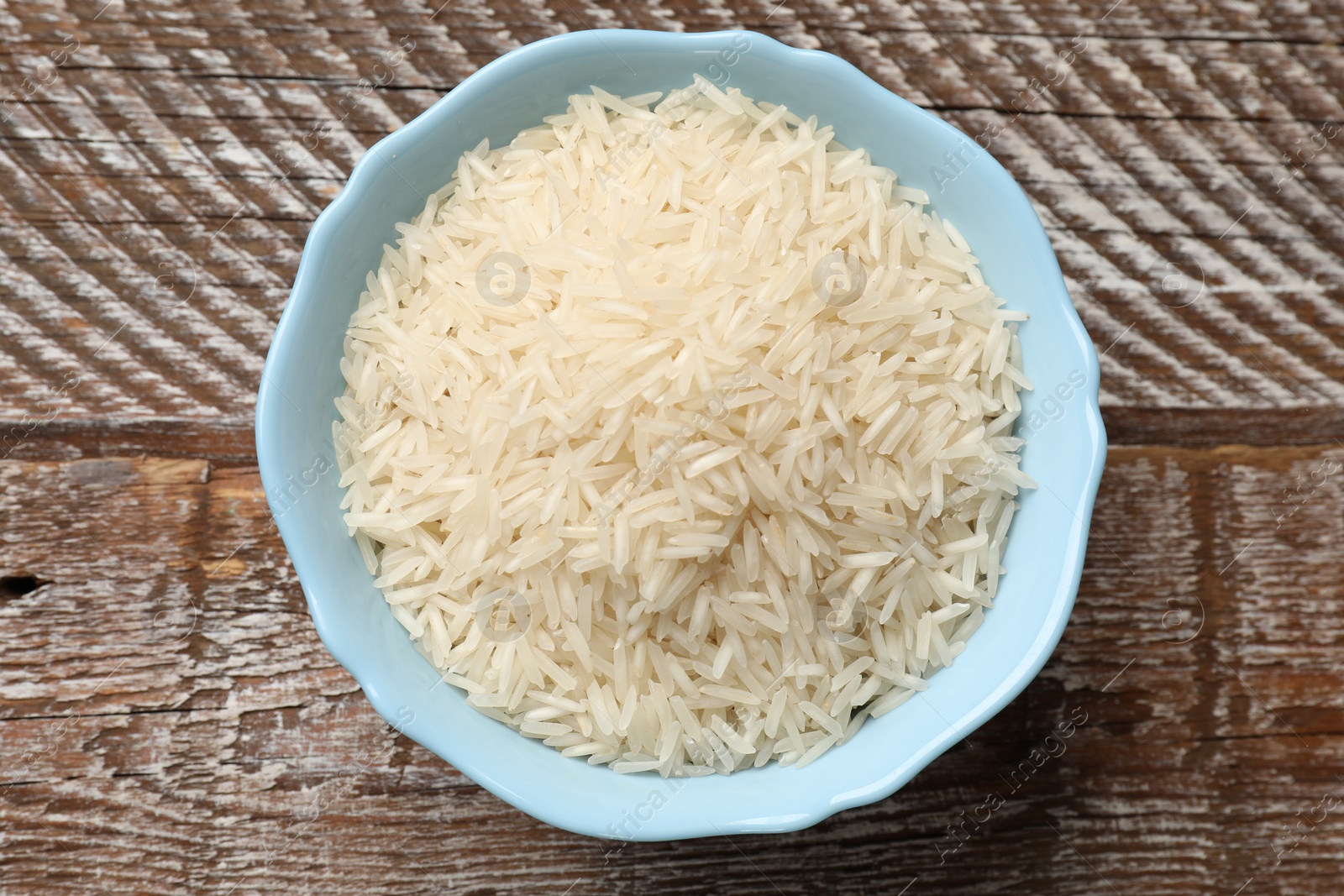 Photo of Raw basmati rice in bowl on wooden table, top view