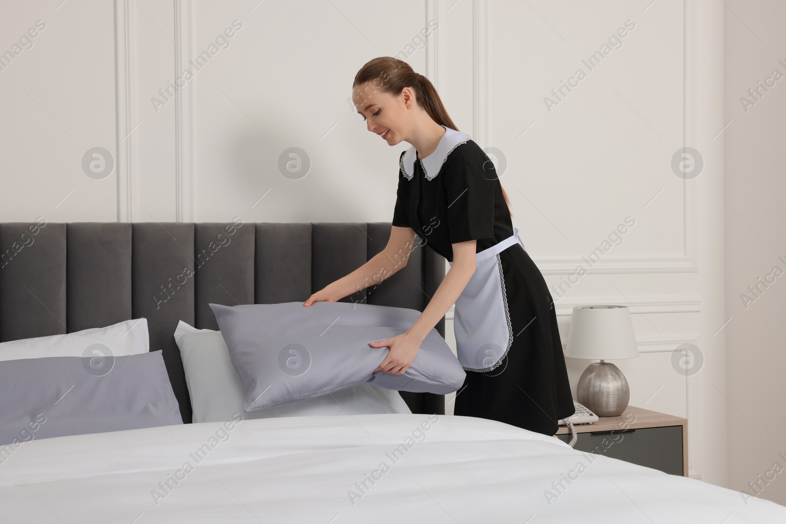 Photo of Young maid making bed in hotel room