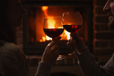 Photo of Couple with glasses of red wine near burning fireplace, closeup