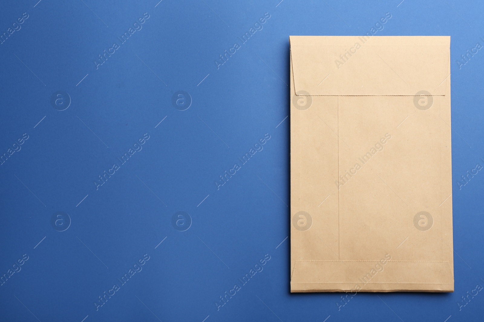 Photo of Kraft paper envelope on blue background, top view. Space for text