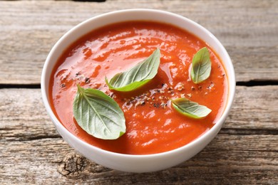 Photo of Delicious tomato soup with basil and spices on wooden table, closeup