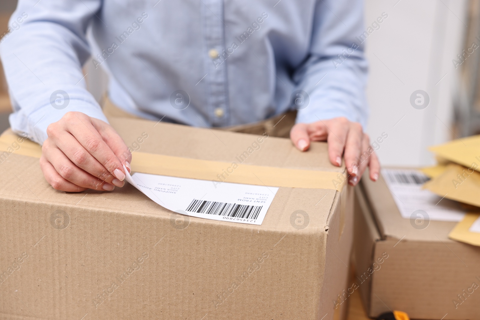 Photo of Parcel packing. Post office worker sticking barcode on box indoors, closeup