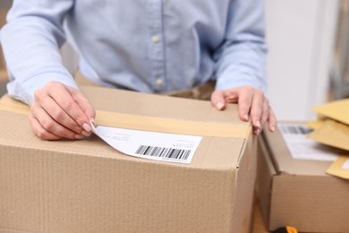 Parcel packing. Post office worker sticking barcode on box indoors, closeup