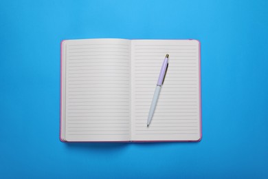 Photo of Open notebook and pen on light blue background, top view