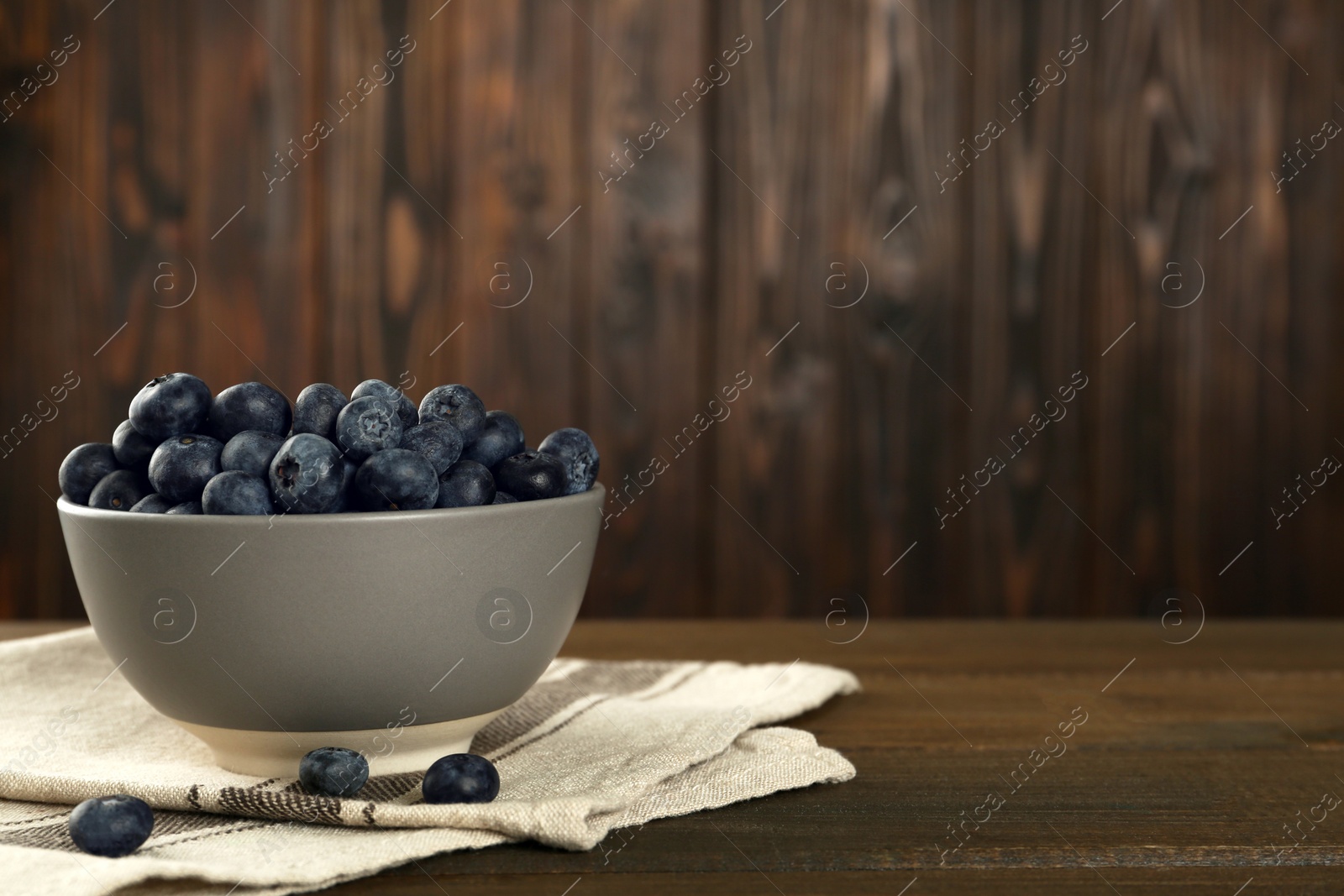 Photo of Ceramic bowl with blueberries on wooden table, space for text. Cooking utensil