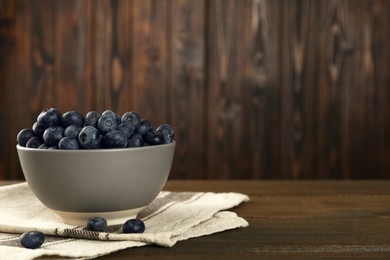Photo of Ceramic bowl with blueberries on wooden table, space for text. Cooking utensil