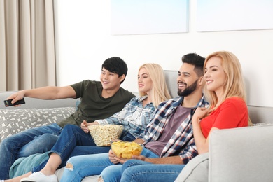 Photo of Young people with snacks watching TV on sofa at home