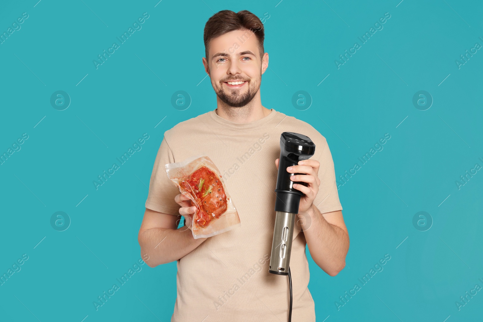Photo of Smiling man holding sous vide cooker and meat in vacuum pack on light blue background