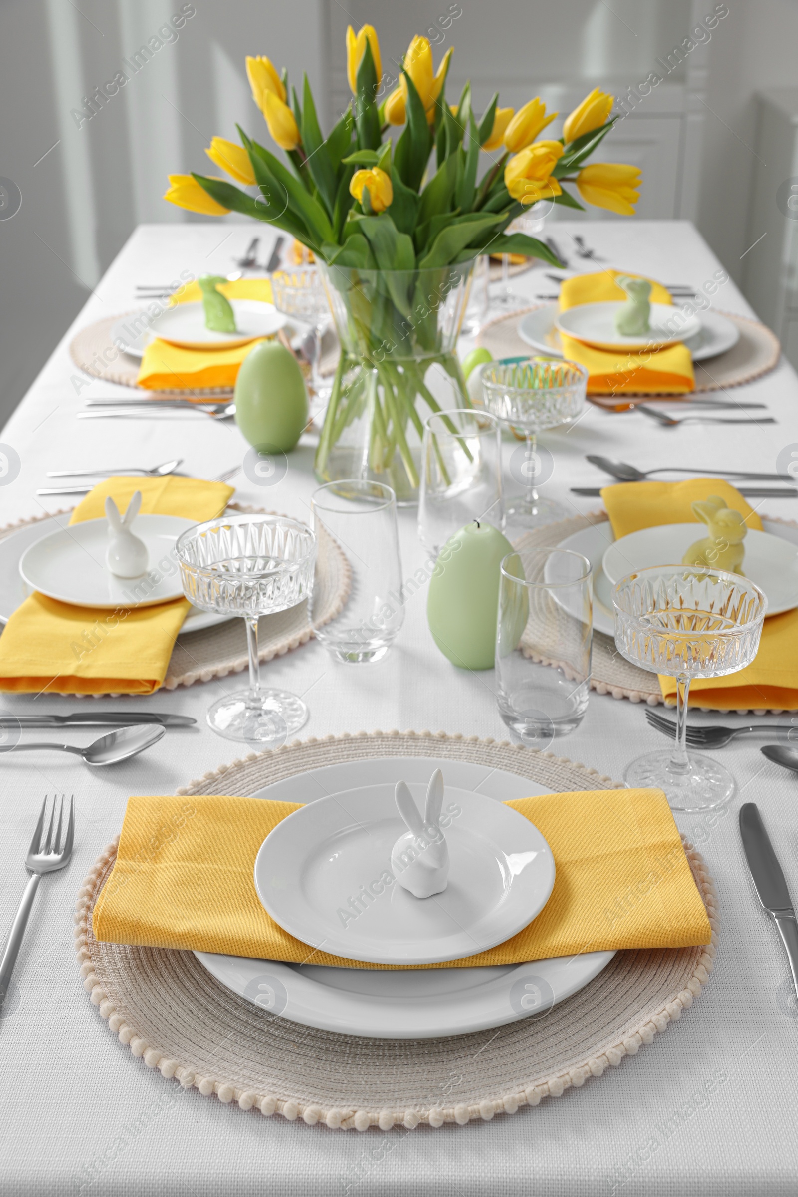 Photo of Festive table setting with glasses, painted eggs and vase of tulips. Easter celebration