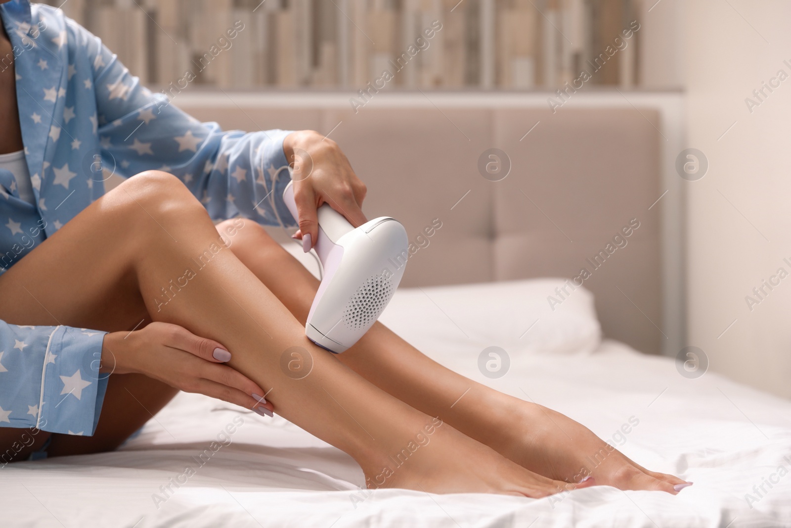 Image of Young woman epilating her legs in bedroom, closeup