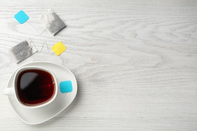 Photo of Tea bags in ceramic cup of hot water on white wooden table, flat lay. Space for text