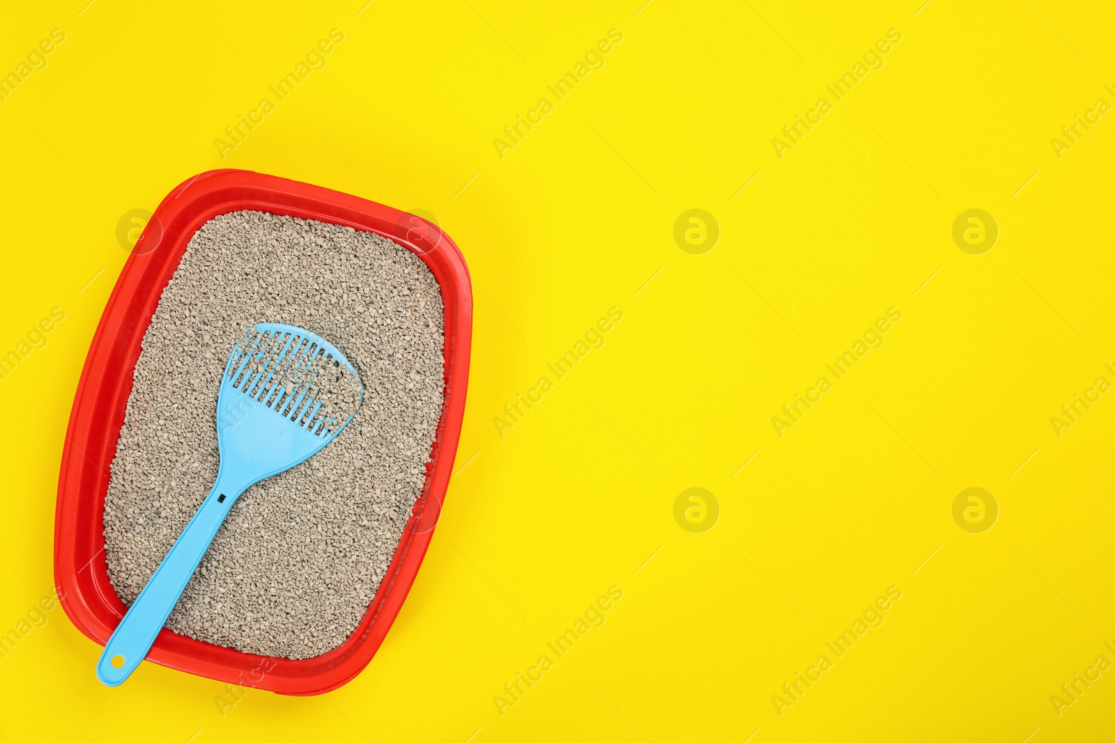 Photo of Cat litter tray with filler and scoop on yellow background, top view. Space for text