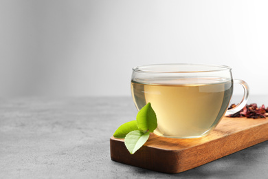 Photo of Cup of green tea and leaves on grey table. Space for text