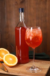 Photo of Aperol spritz cocktail and ice cubes in glass and bottle on wooden table