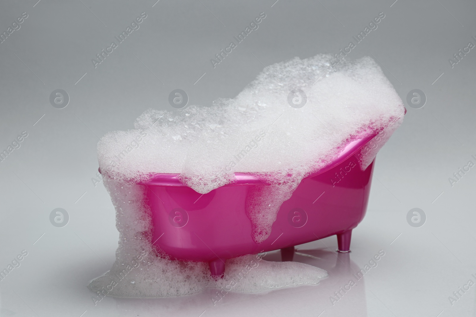 Photo of Toy bathtub overflowing with foam on grey background