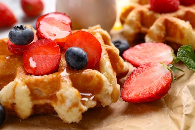 Photo of Delicious Belgian waffle with fresh berries and honey on parchment paper, closeup