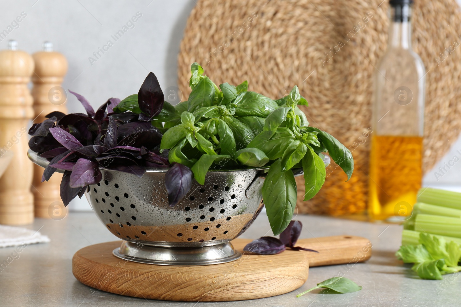 Photo of Metal colander with different fresh basil leaves on grey countertop