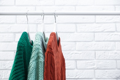 Collection of warm sweaters hanging on rack near brick wall, closeup. Space for text