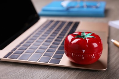Kitchen timer in shape of tomato and laptop on wooden table, closeup. Space for text