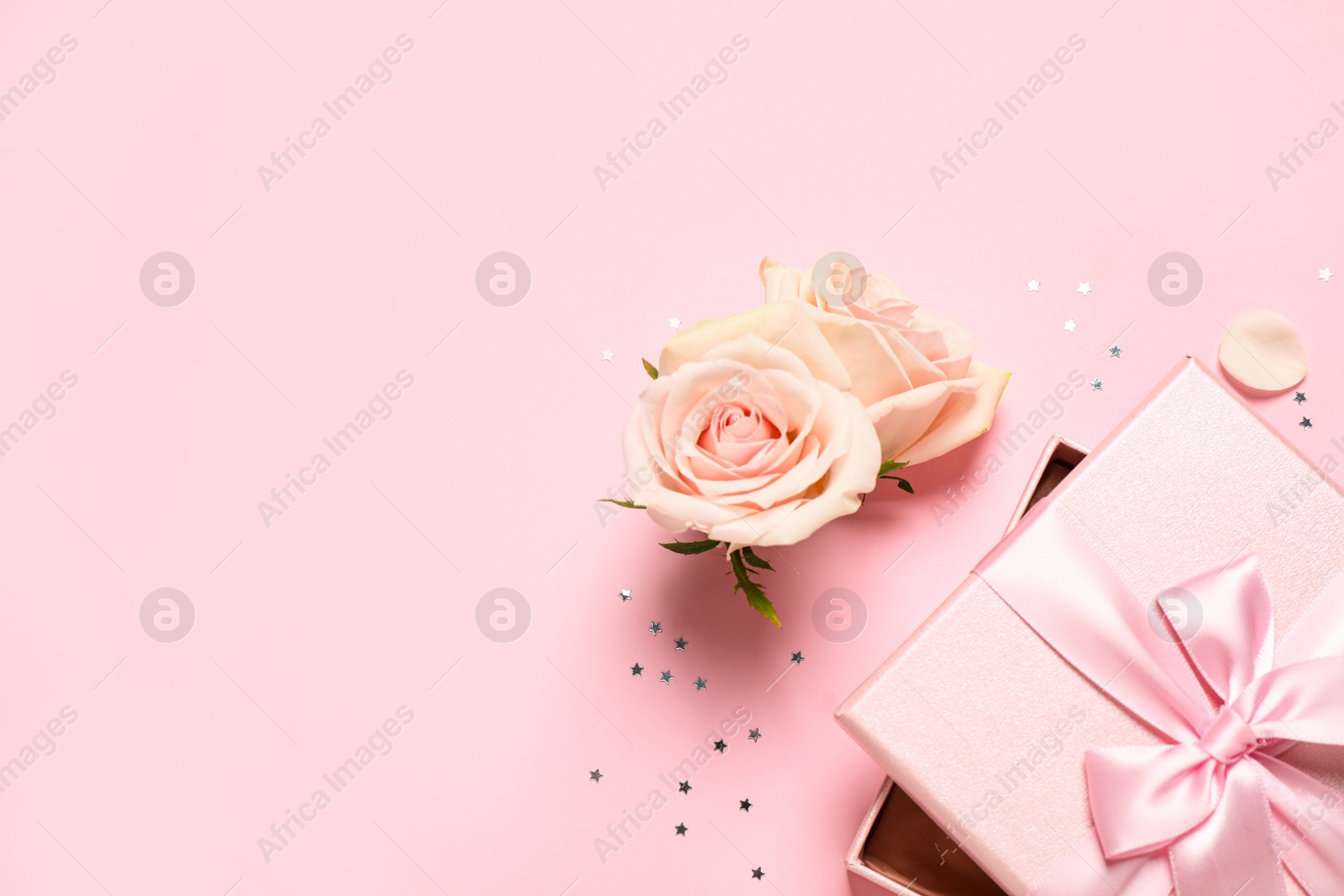 Photo of Elegant gift box, beautiful flowers and confetti on pink background, flat lay. Space for text