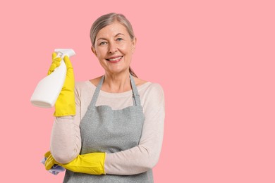 Photo of Happy housewife with spray bottle and rag on pink background, space for text