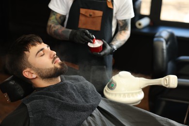 Photo of Professional hairdresser with shaving foam near bearded client in barbershop