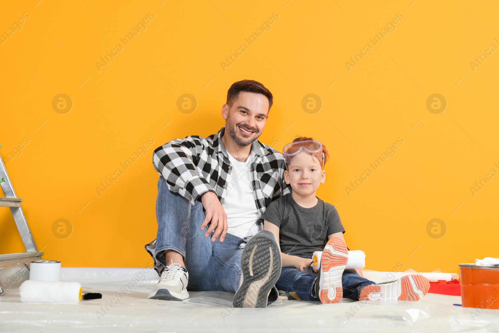Photo of Father and son with repair tools near orange wall