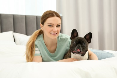 Photo of Happy woman hugging with cute French Bulldog on bed in room