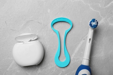 Tongue cleaner, dental floss and electric toothbrush on grey background, flat lay