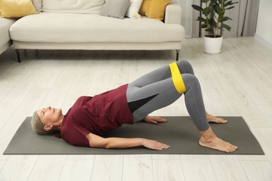 Photo of Senior woman doing exercise with fitness elastic band on mat at home