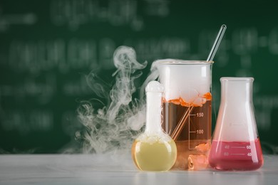 Photo of Laboratory glassware with colorful liquids on white table, space for text. Chemical reaction
