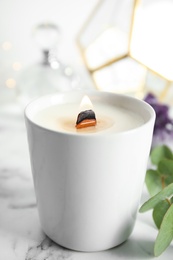 Burning candle with wooden wick on white marble table