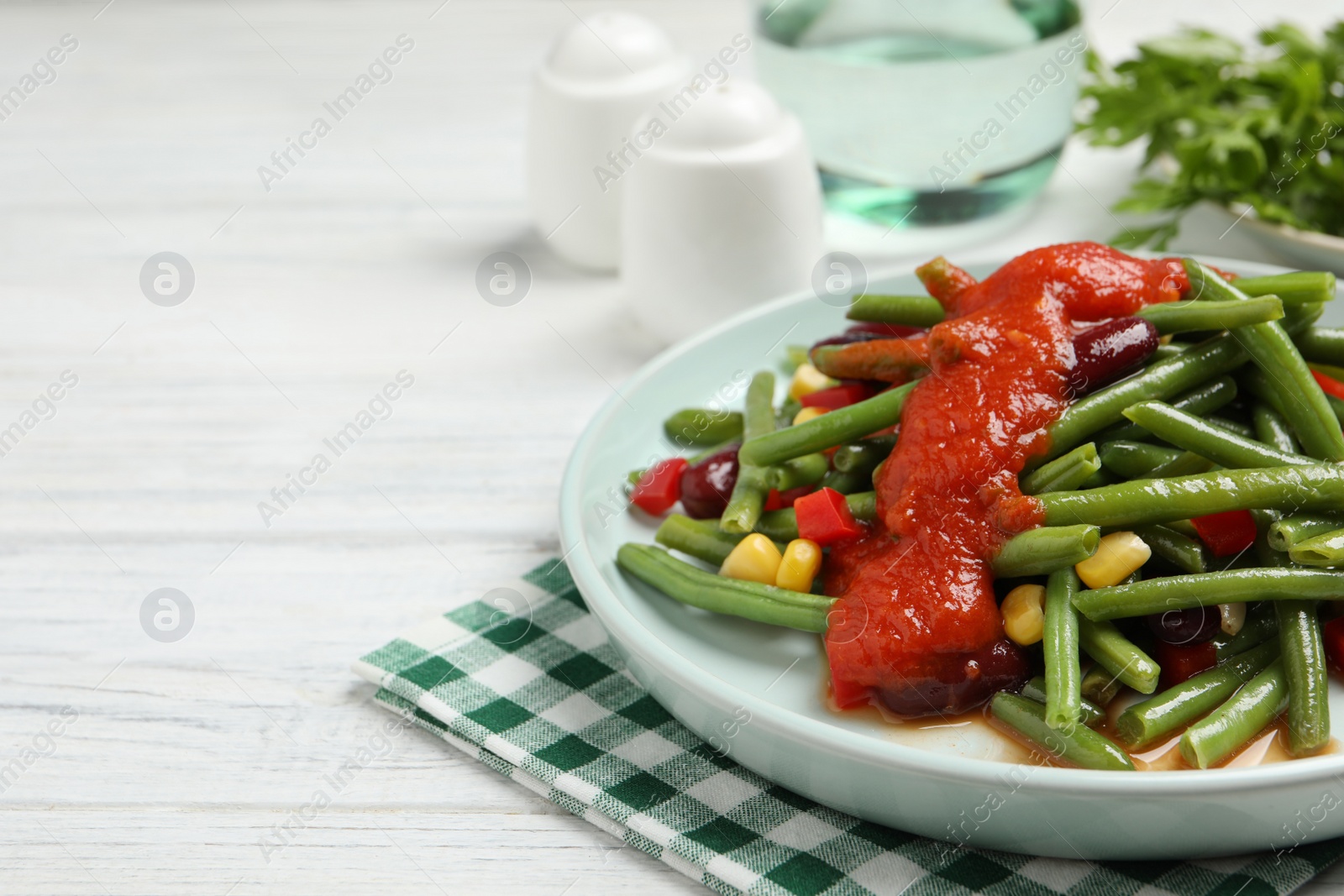 Photo of Delicious salad with green beans and tomato sauce served on white wooden table, closeup. Space for text