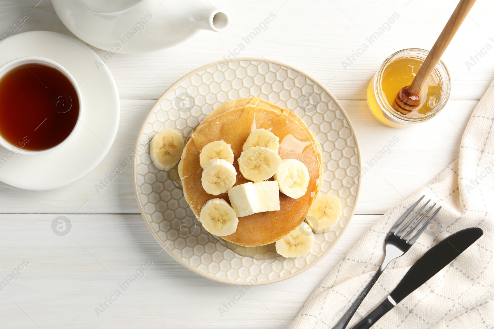 Photo of Delicious pancakes with bananas, honey and butter served with tea on white wooden table, flat lay