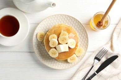Photo of Delicious pancakes with bananas, honey and butter served with tea on white wooden table, flat lay