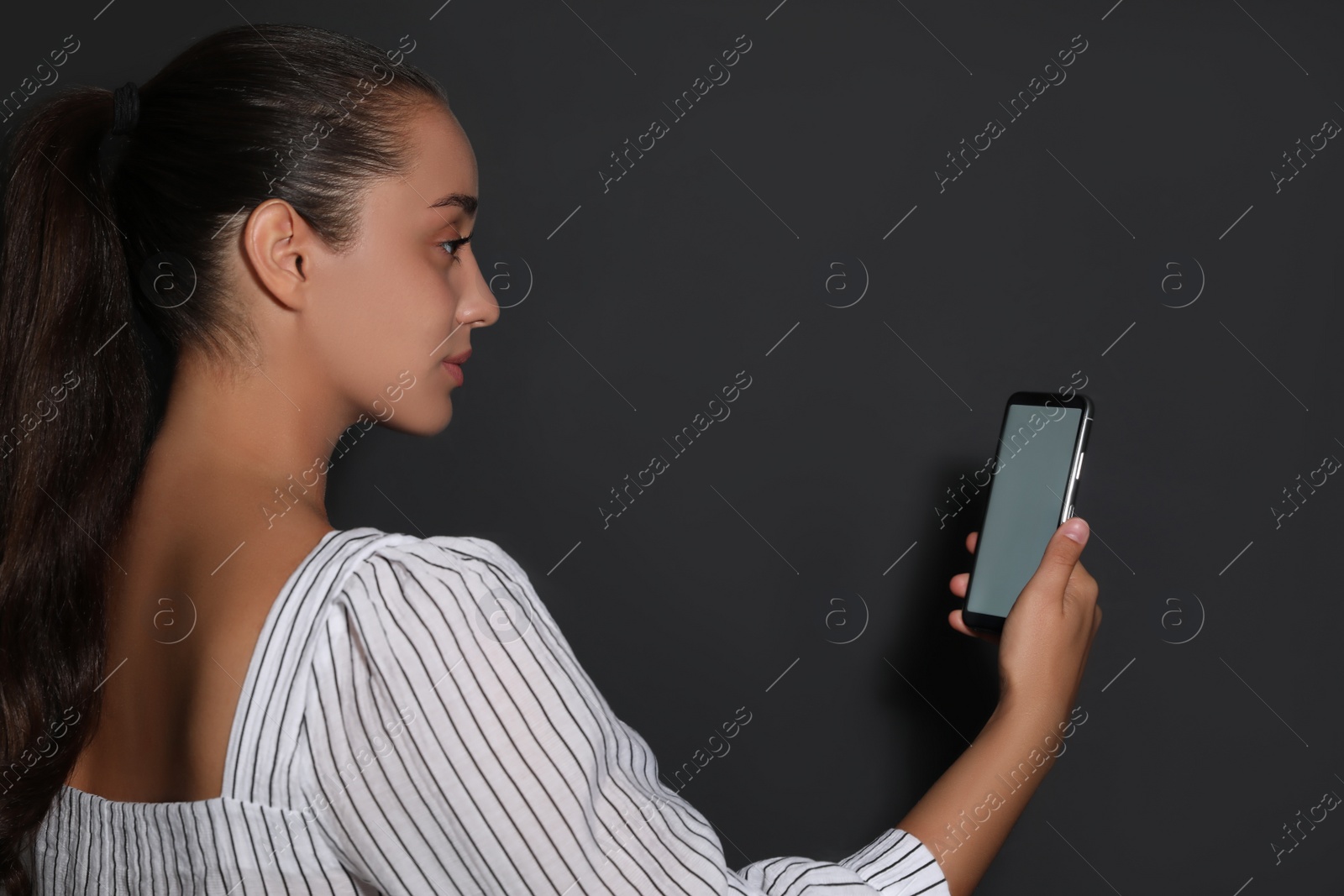 Photo of Young woman unlocking smartphone with facial scanner on black background. Biometric verification