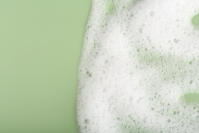 White fluffy foam on green background, top view. Space for text