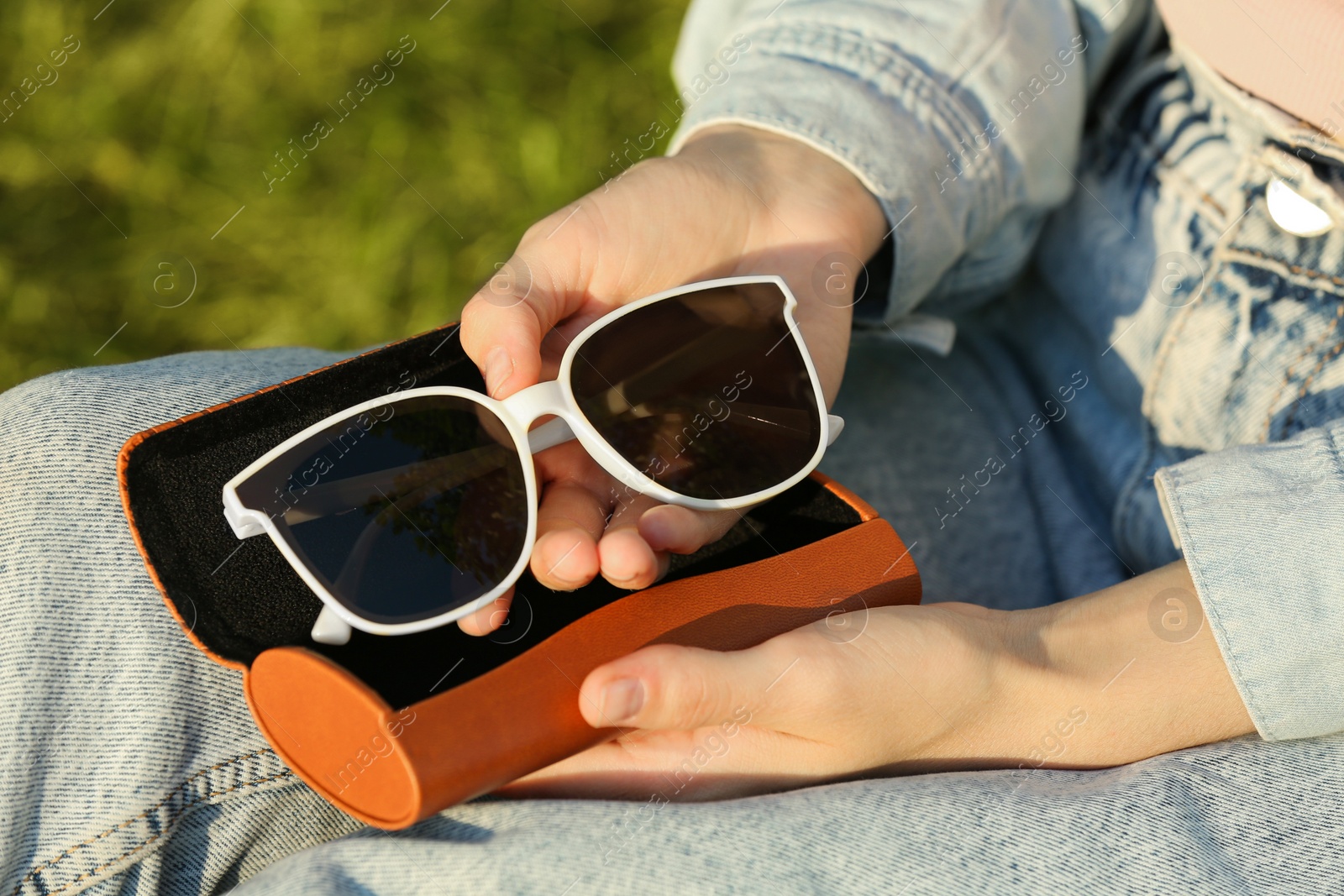 Photo of Woman holding sunglasses in brown leather case outdoors on sunny day, closeup