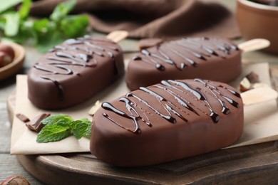 Photo of Delicious glazed ice cream bars and mint on wooden board, closeup