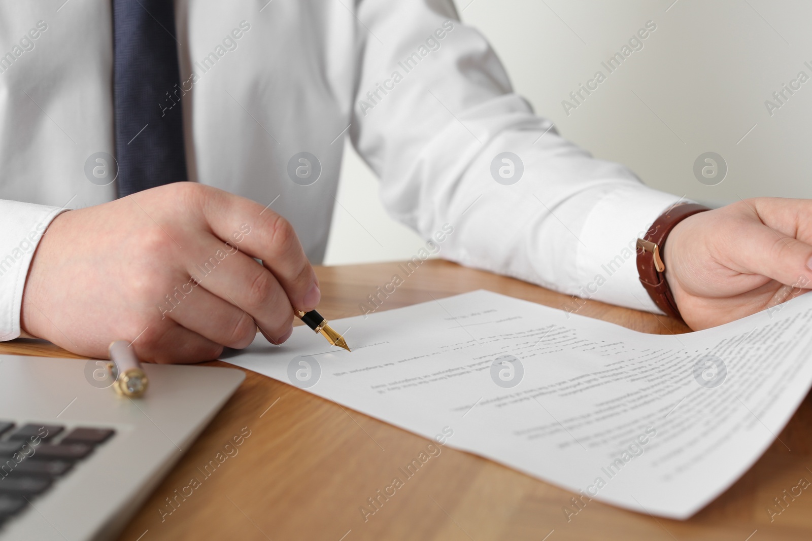 Photo of Notary signing document at wooden table, closeup