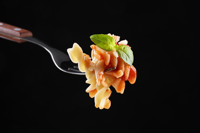 Photo of Delicious fusilli pasta with tomato sauce on fork against  black background