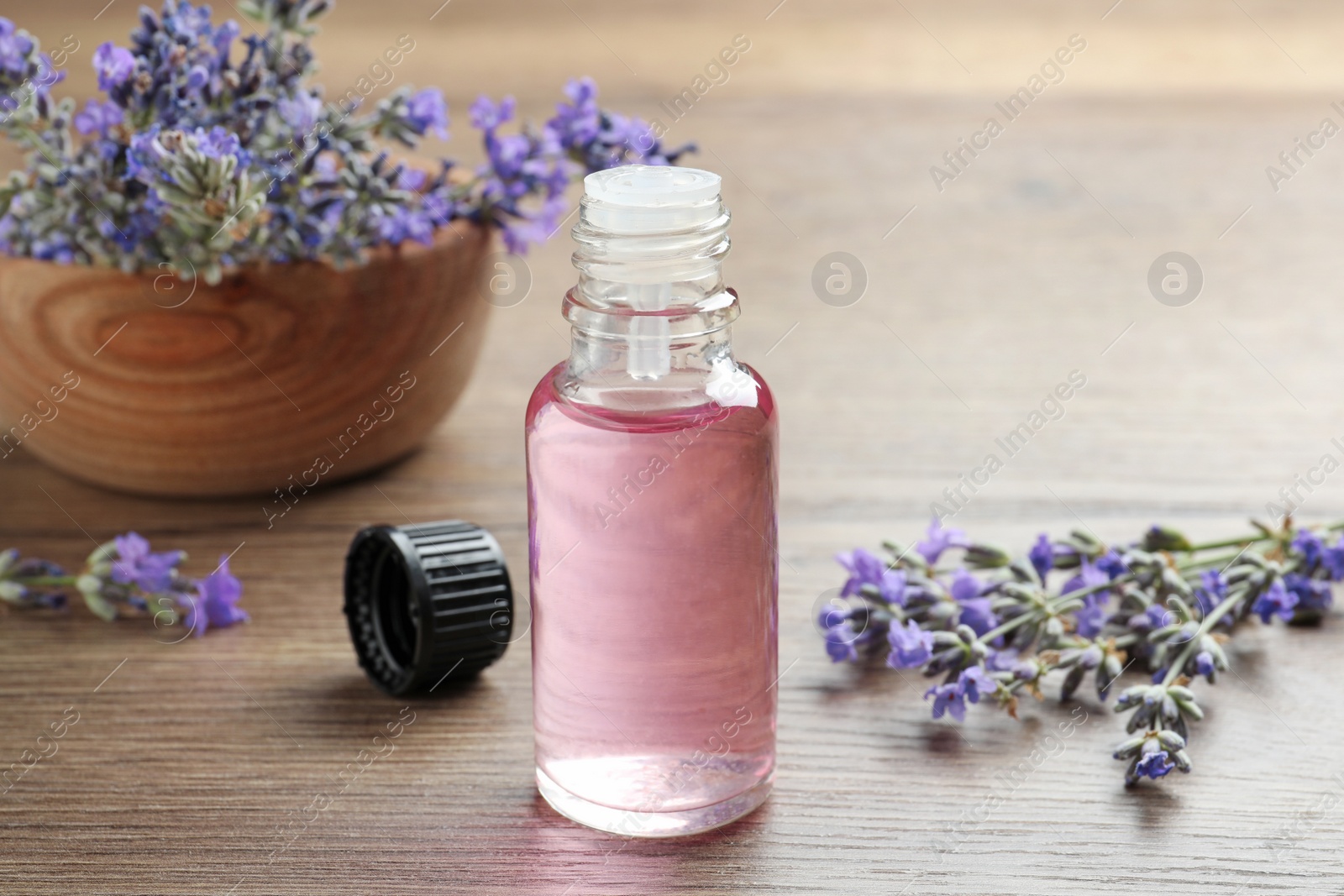 Photo of Bottle of essential oil and lavender flowers on wooden table